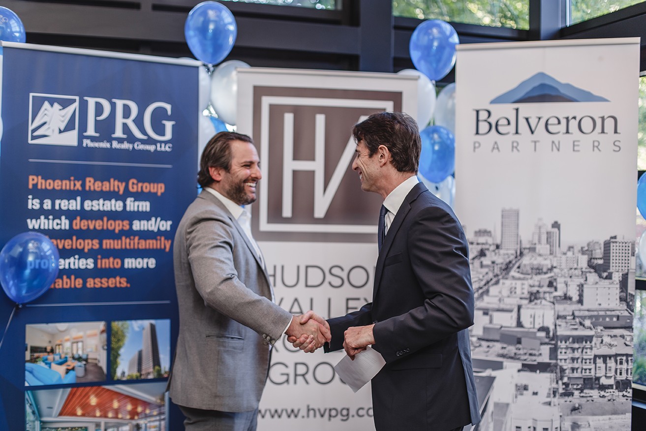 Executives shaking hands in front of sponsor banners at a corporate event, by Josh Mak Photography